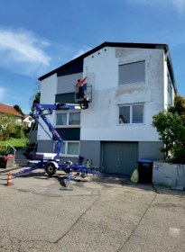 Hausfassade mit fleckigem Anstrich, davor eine Arbeitsbühne